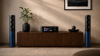 Audio equipment including speakers and a receiver on a wooden cabinet against a beige wall.