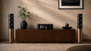 Audio equipment including speakers and a receiver on a wooden cabinet against a beige wall.